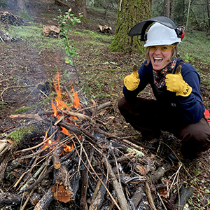 Student next to controlled fire in forest 